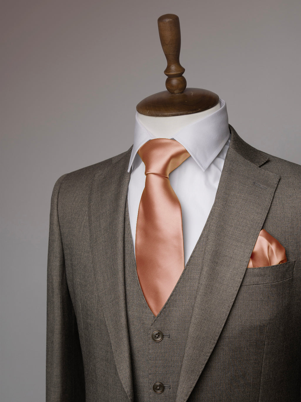 Gray suit with a white shirt and copper pink tie on a mannequin against a gray background