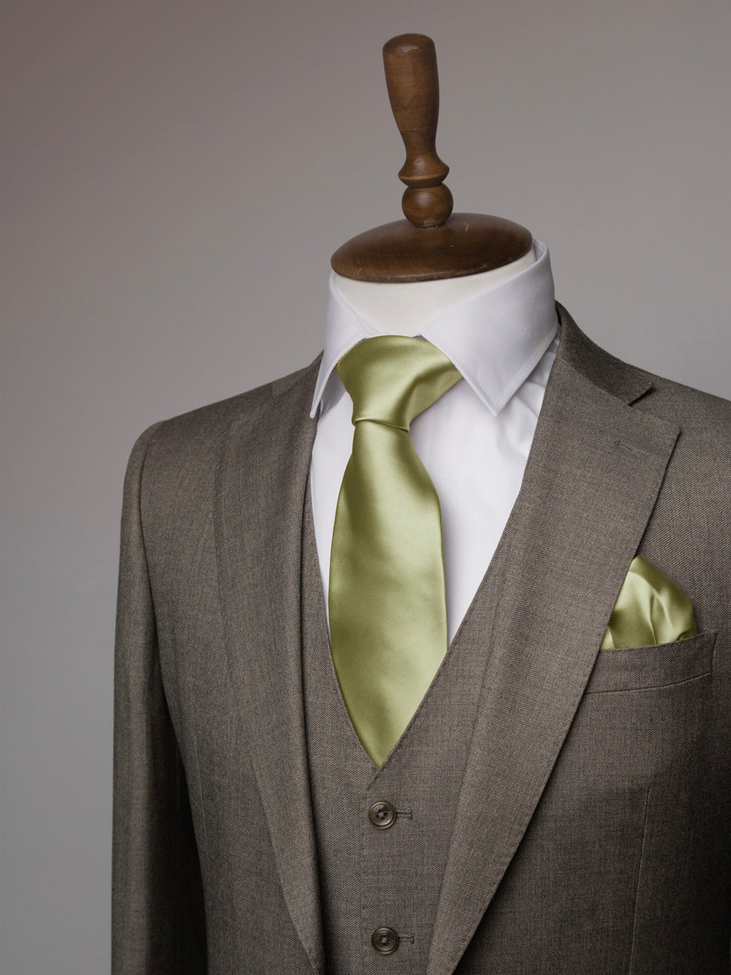 Taupe suit with a white shirt and pistachio tie on a mannequin against a gray background