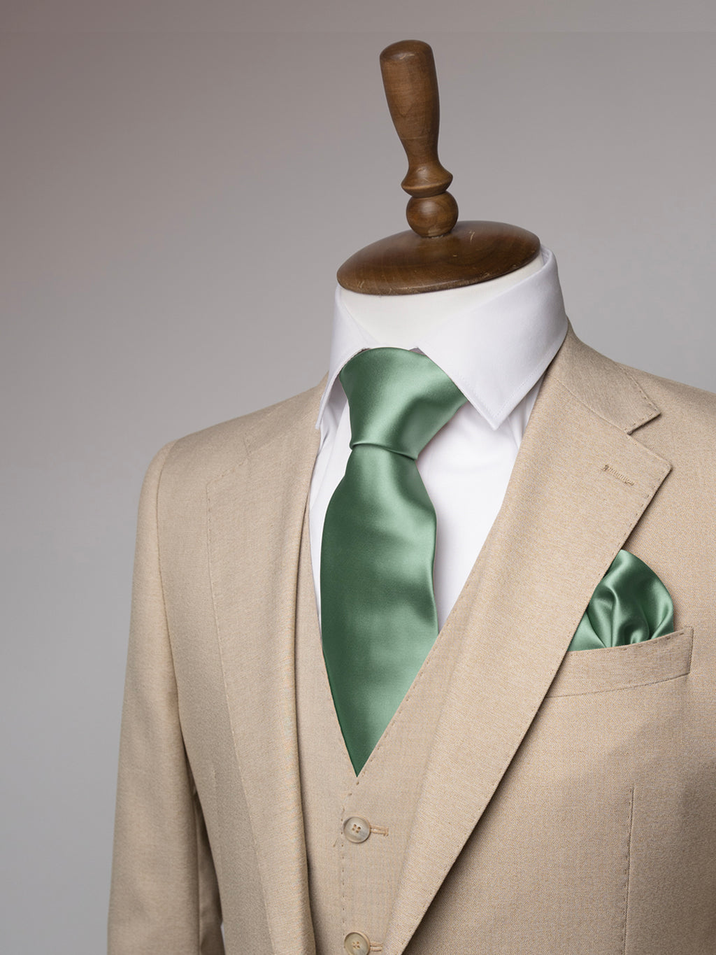 Cream suit with a white shirt and sage green tie on a mannequin against a gray background