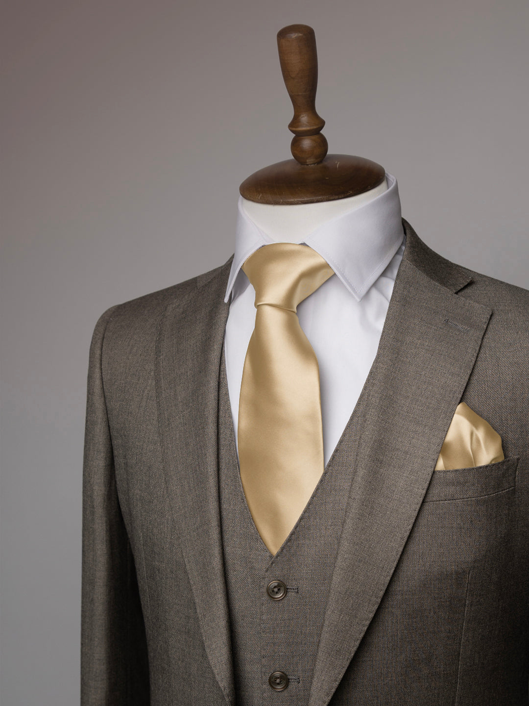 Taupe suit with sand tie and pocket square on a mannequin against a gray background