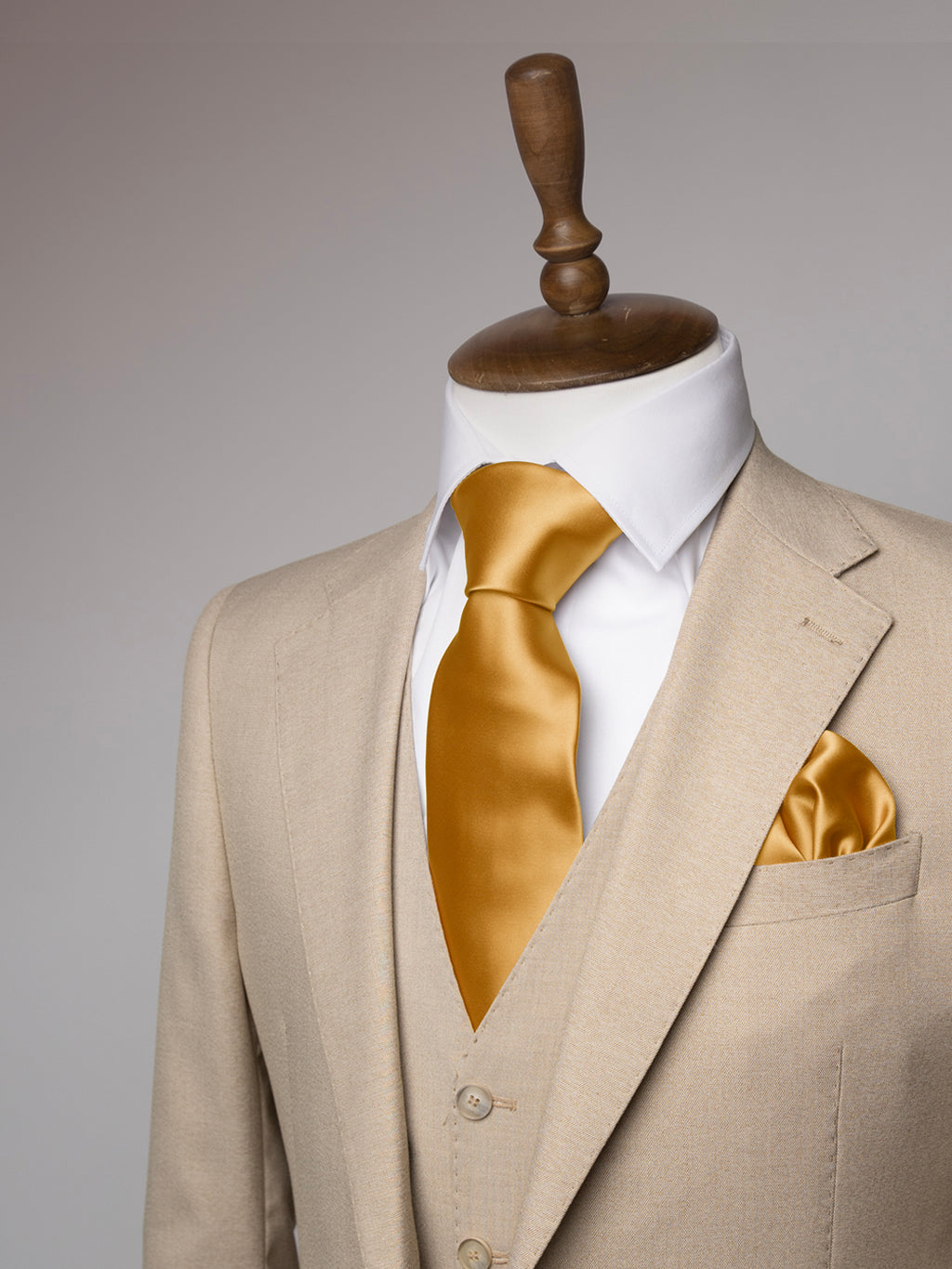 Cream suit with a sand stone tie and pocket square on a mannequin against a gray background