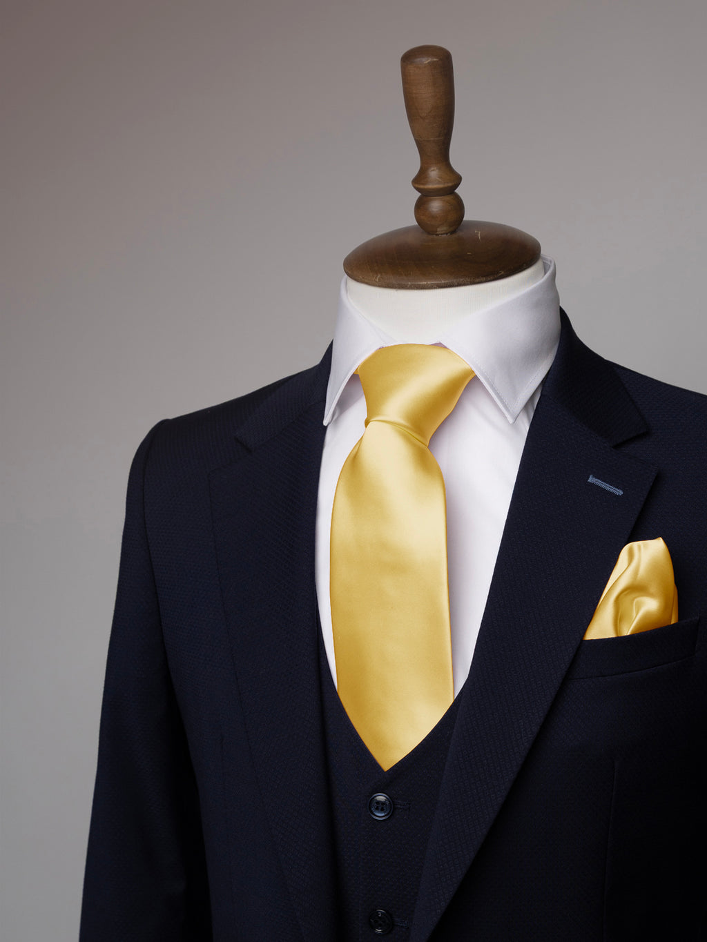 Mannequin wearing a navy suit with a white shirt and lemon tie and pocket square on a gray background