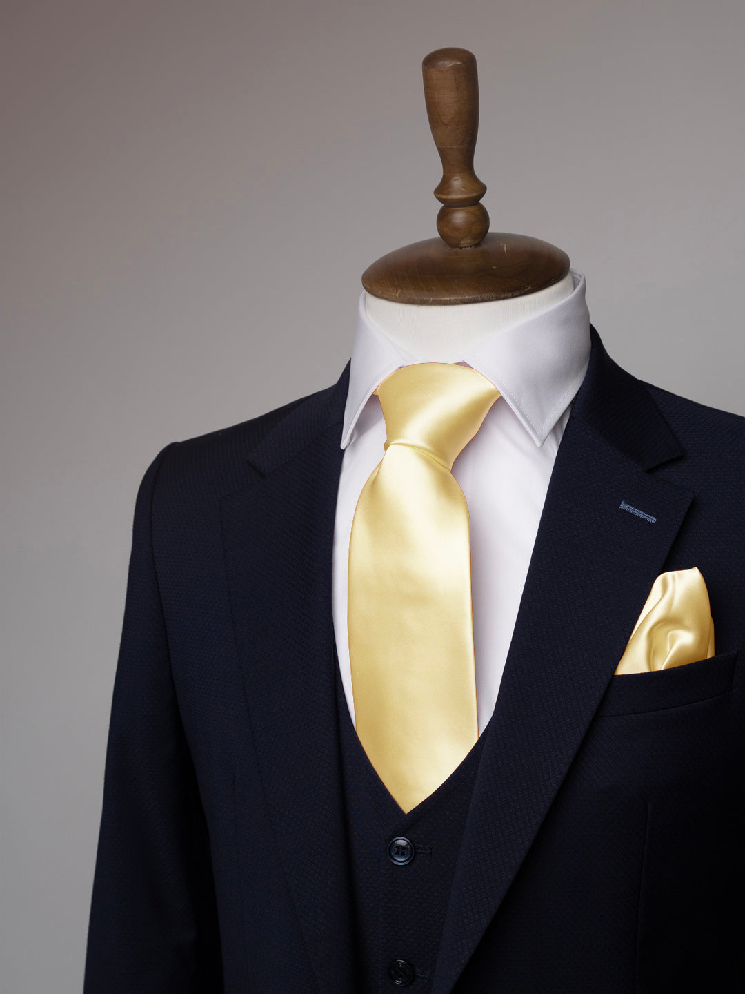 Navy suit with a white shirt, gold tie, and matching pocket square on a mannequin against a gray background.