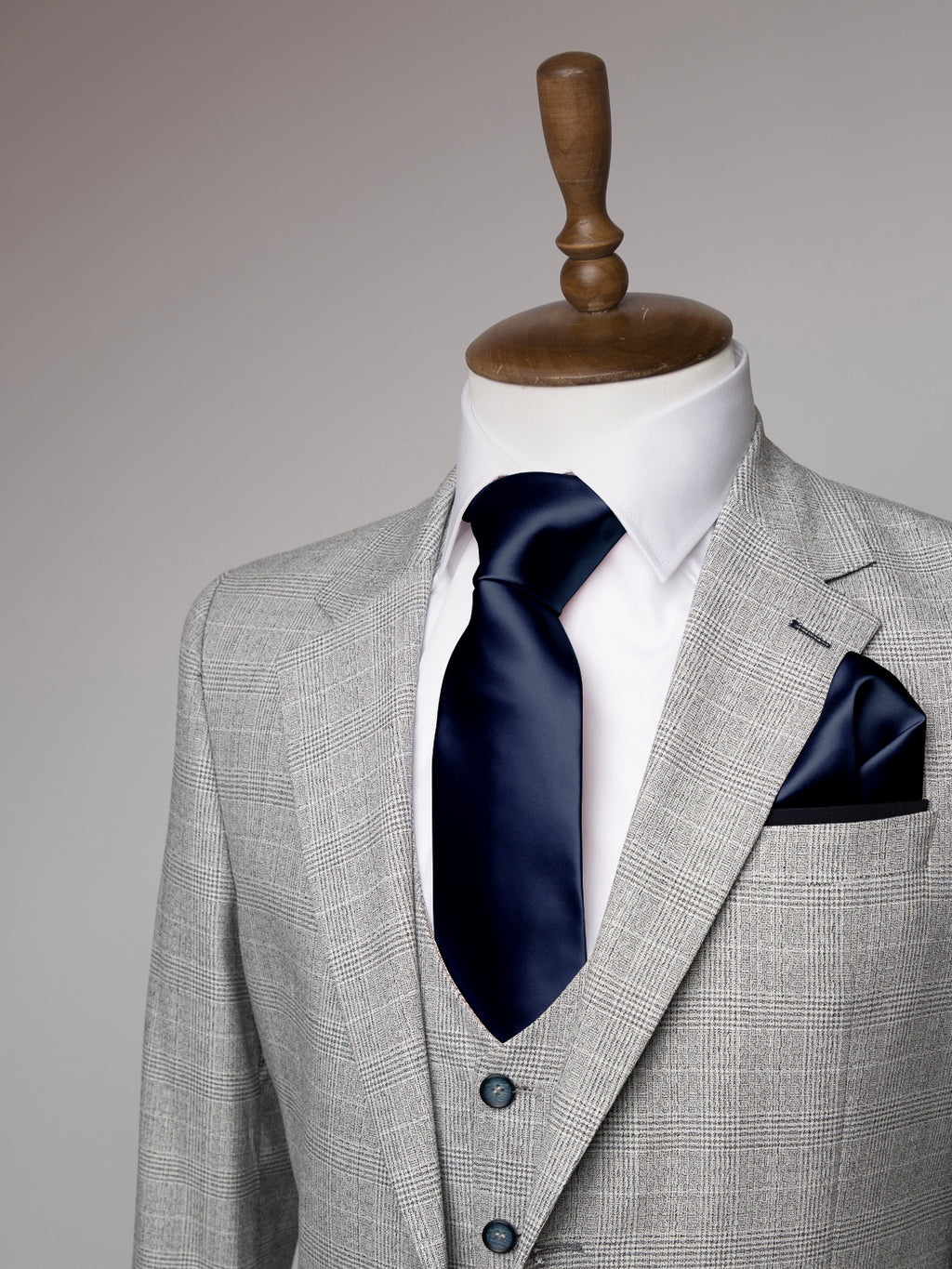 Gray suit with navy tie and pocket square on a mannequin against a gray background
