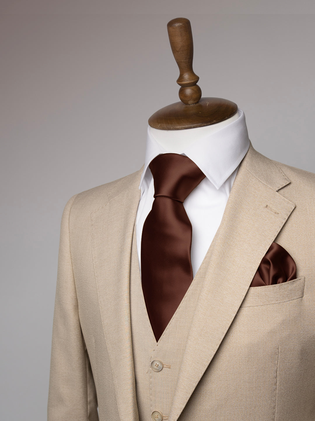 Cream suit with brown tie on a mannequin against a gray background